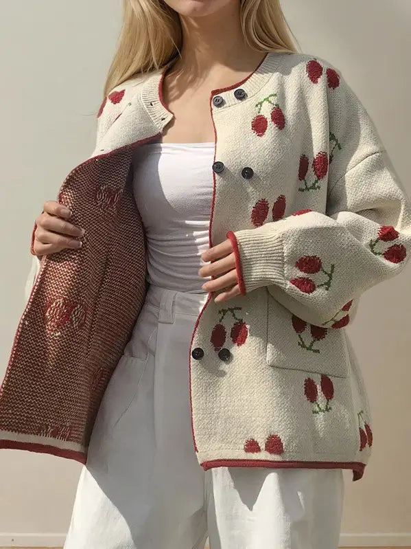 Person wearing a white cardigan with red berry patterns on a plain background