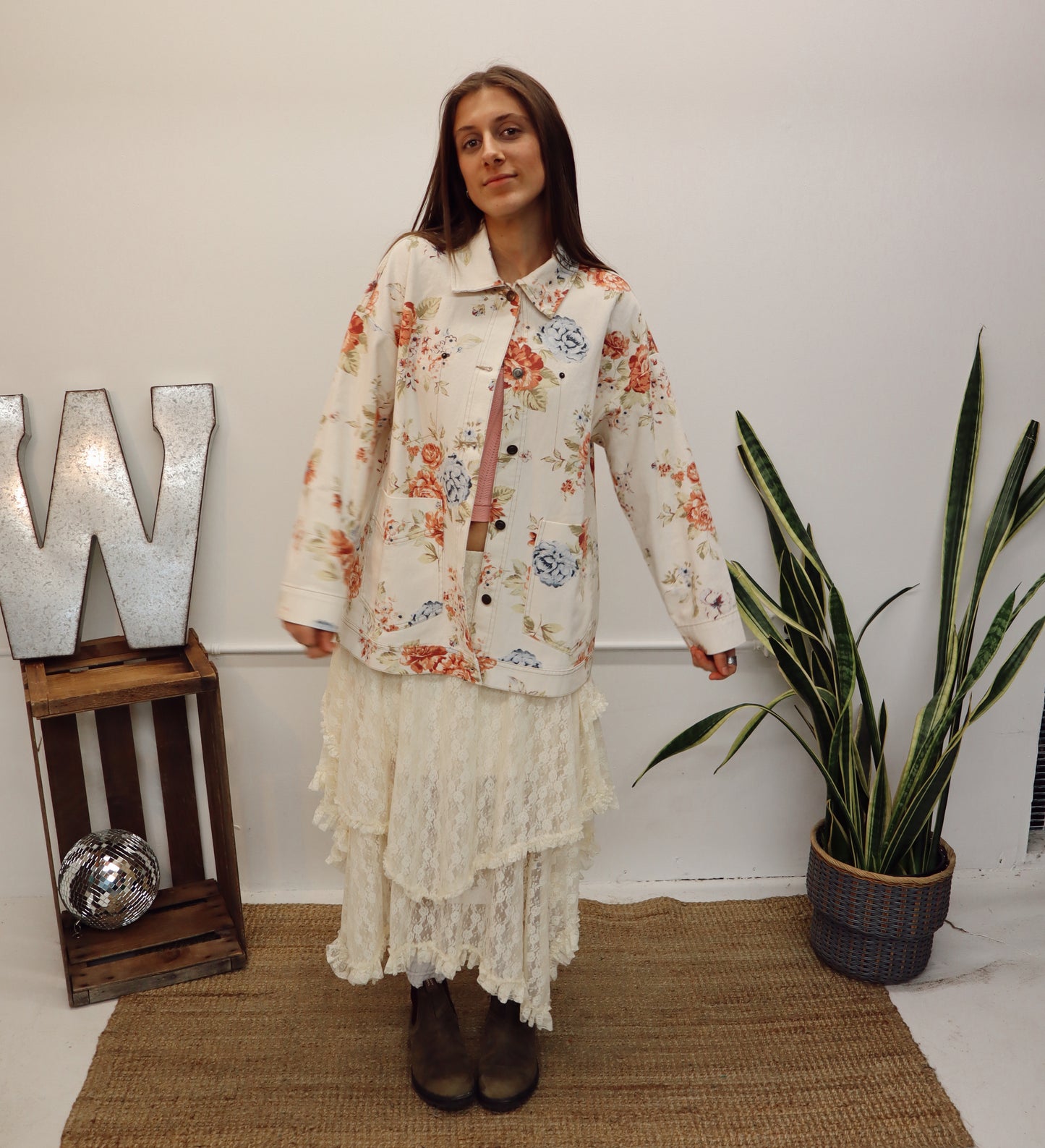 Woman in a floral dress standing in a room with a plant and decorative elements.