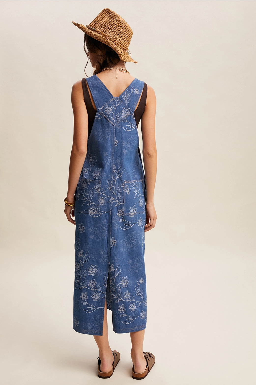 Woman wearing a blue floral jumpsuit and straw hat on a beige background
