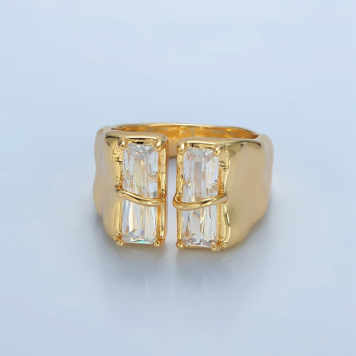 Gold ring with two large rectangular gemstones on a light blue background