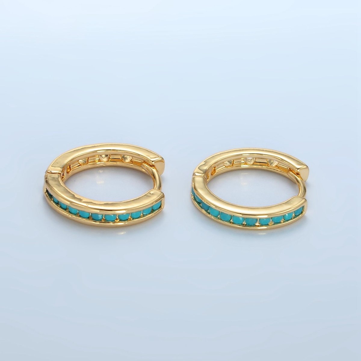 Gold hoop earrings with turquoise stones on a light blue background