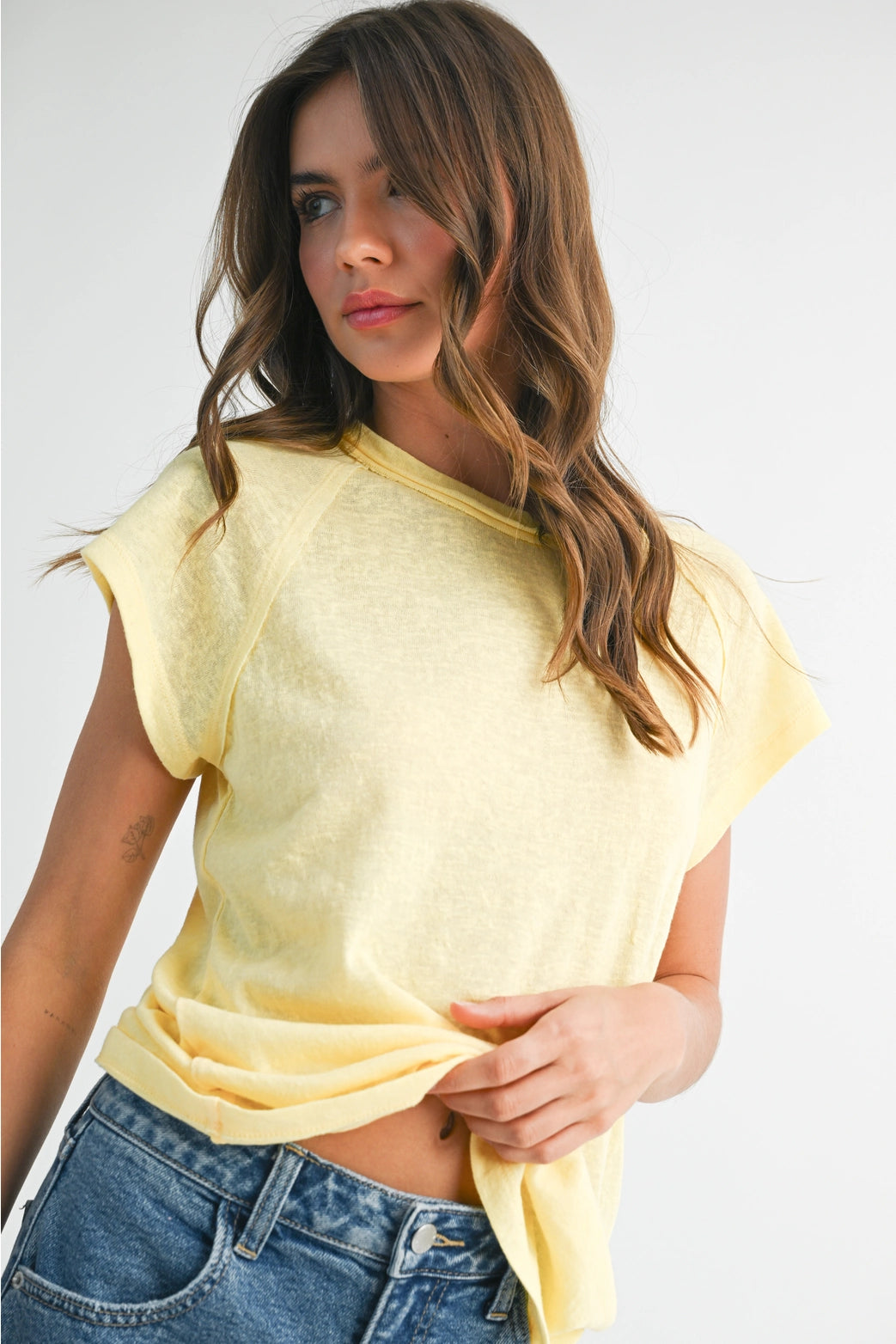 Woman wearing a yellow crop top and blue jeans against a white background