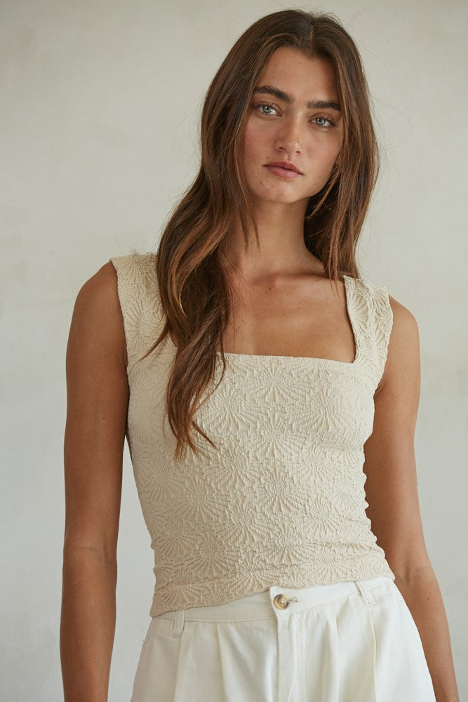 Woman wearing a beige sleeveless top against a plain background