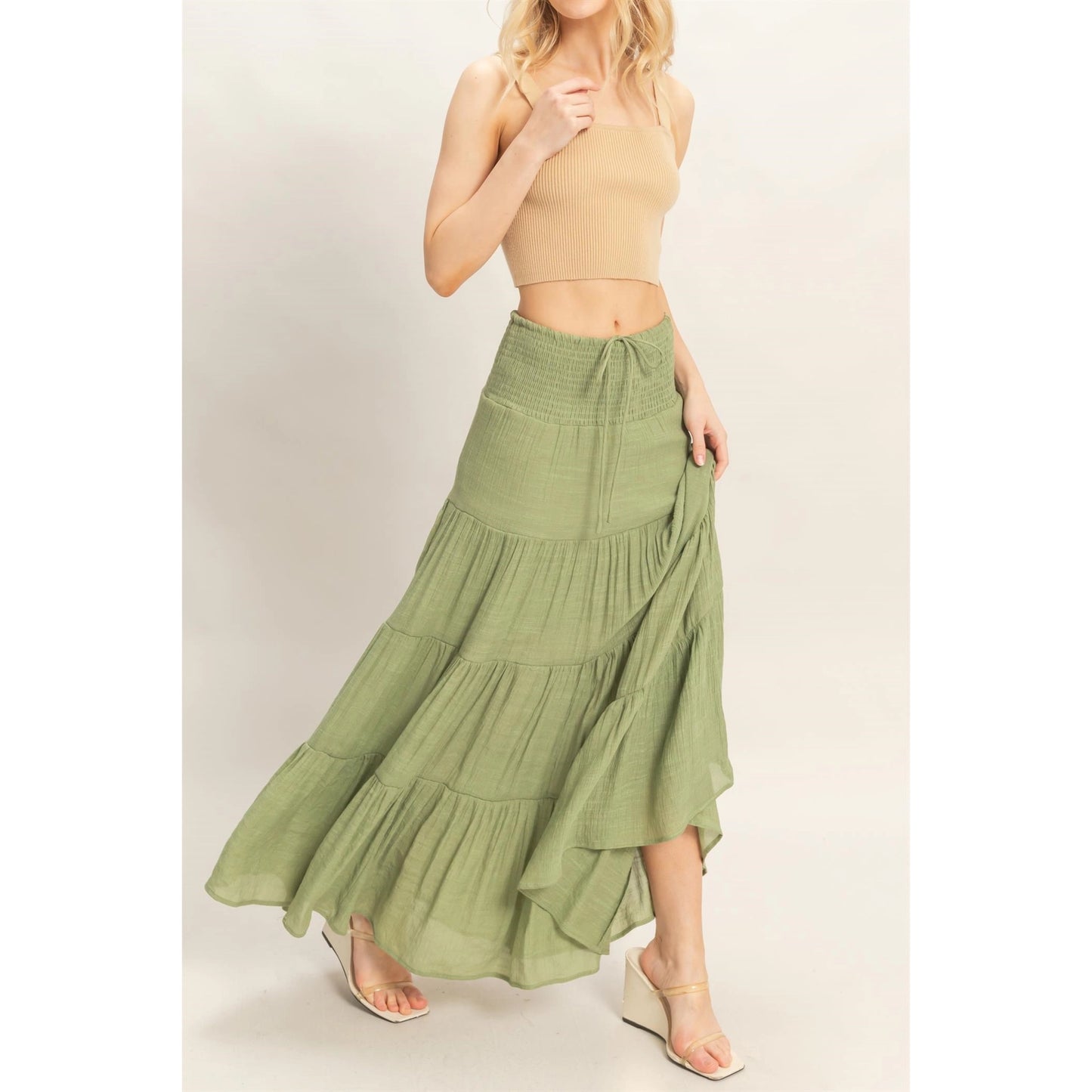 Woman wearing a green tiered skirt and beige top on a light background